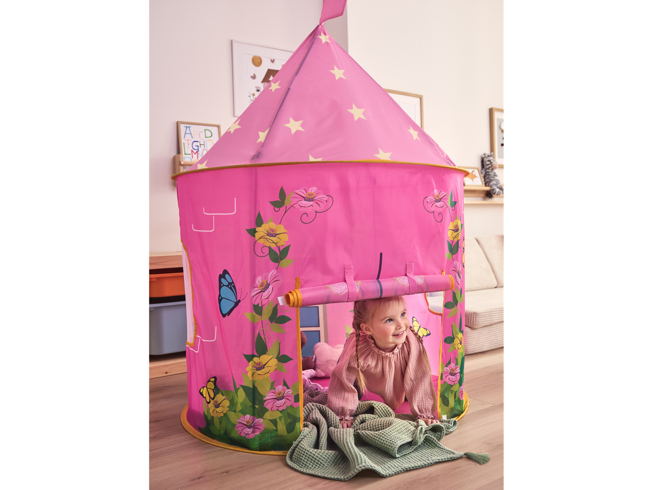 Розова палатка Lupilu® с мотиви на цветя и пеперуди, с усмихнато малко момиченце вътре.