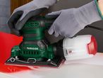 Close-up of a person using a Parkside brand electric sander on a red surface.