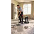 Homem a limpar sujidade molhada do chão com um aspirador de líquidos/sólidos numa divisão em renovação.