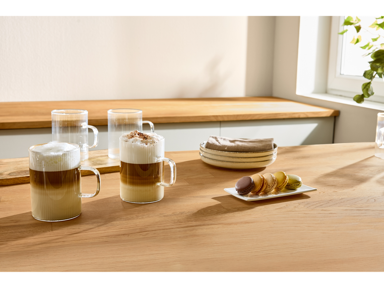 Căni de sticlă cu cafea latte și macarons pe un blat de lemn.