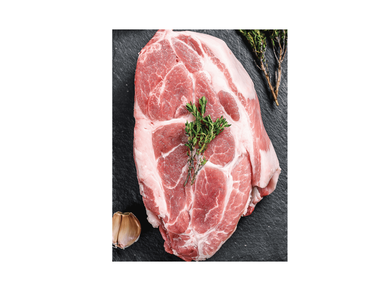 Šviežias kiaulienos sprandinės kepsnys su česnaku ir rozmarinu ant tamsios lentos.