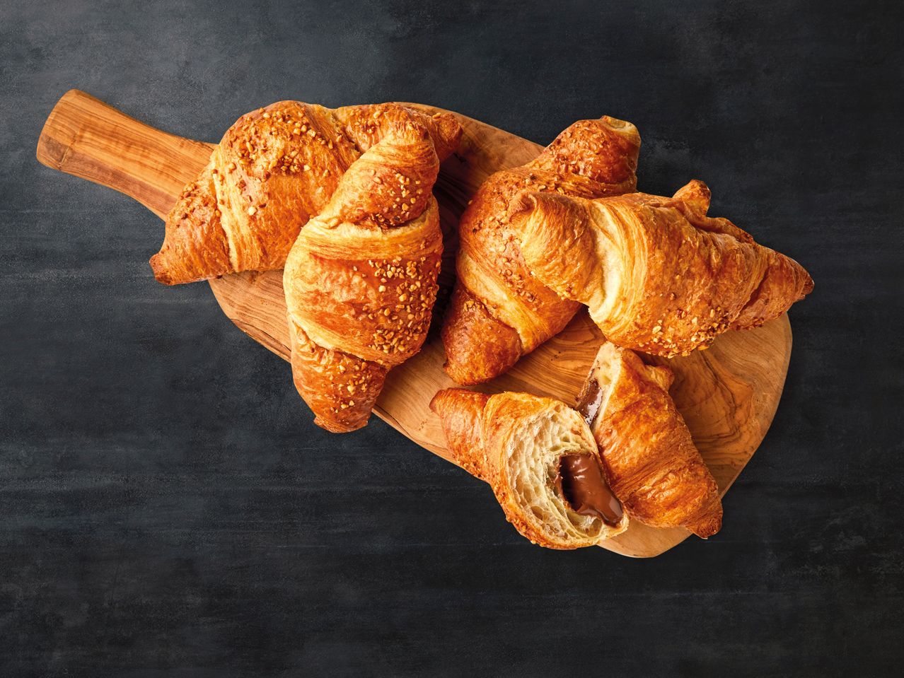Croissants mit Schokolade und Nüssen auf Holzbrett.