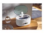 An open ultrasonic cleaner with glasses inside, next to a water carafe and jewelry.