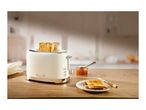 Cream-colored toaster with two slices of toast, jam, and a plate of toast on a wooden table.