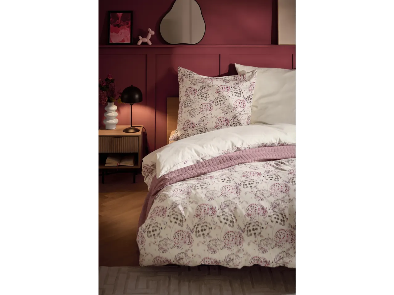 Lenjerie de pat din satin cu model floral și pătură roz pe pat.