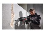 A man using a cordless rotary hammer to chisel a concrete wall.