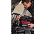 Man jump-starting a car with a portable jump starter, connecting cables to the car battery.