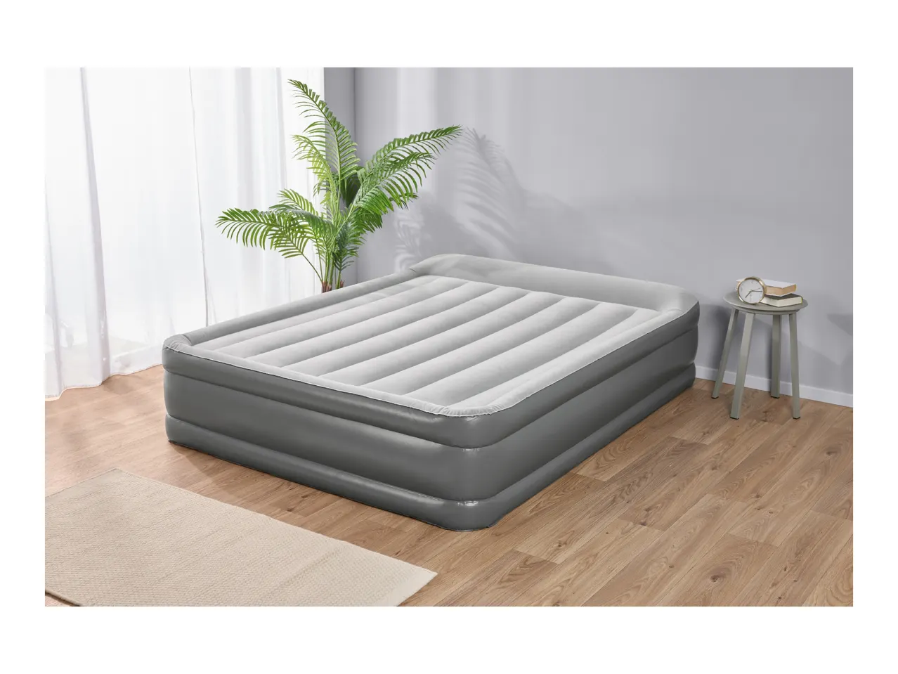 Grey inflatable air mattress in a room with a plant and side table