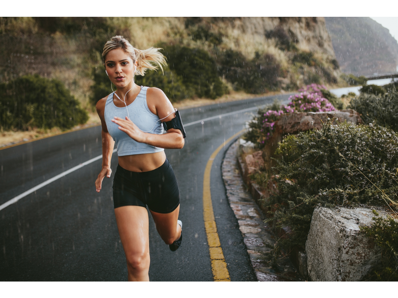 Mulher a correr à chuva com uma braçadeira para telemóvel, ideal para um estilo de vida ativo.
