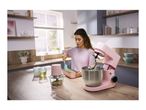Woman baking with a pink stand mixer and food chopper on a wooden kitchen counter.