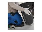 Mechanic kneeling on a knee pad, wearing work gloves, holding a car tire, with an impact wrench nearby.