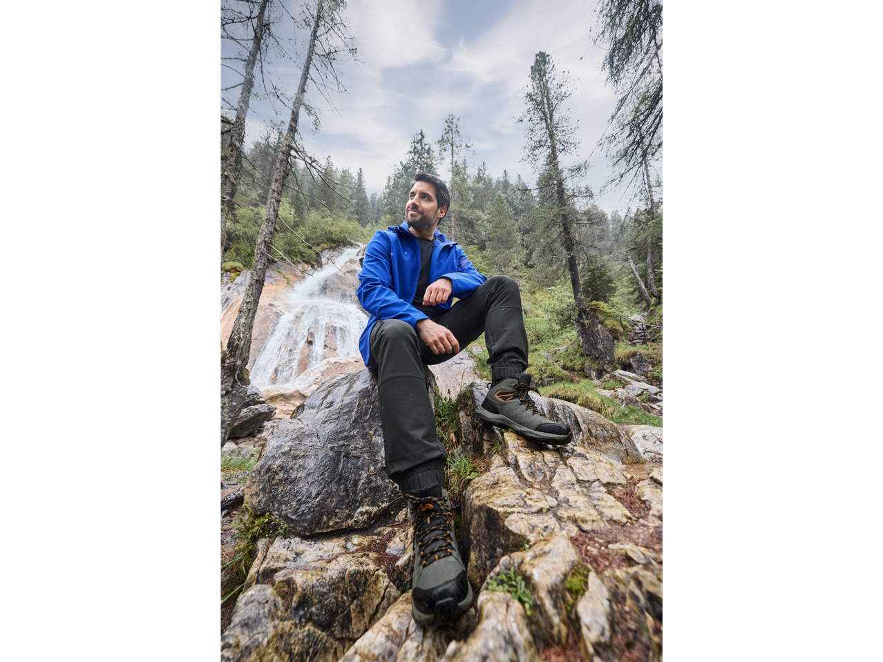 Man in CRIVIT thermal softshell jacket and hiking boots by a waterfall.