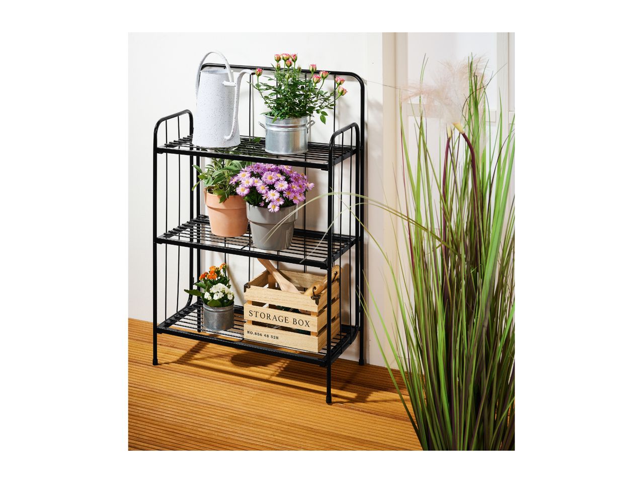 Black metal plant stand with various potted plants, a watering can, and a wooden storage box.