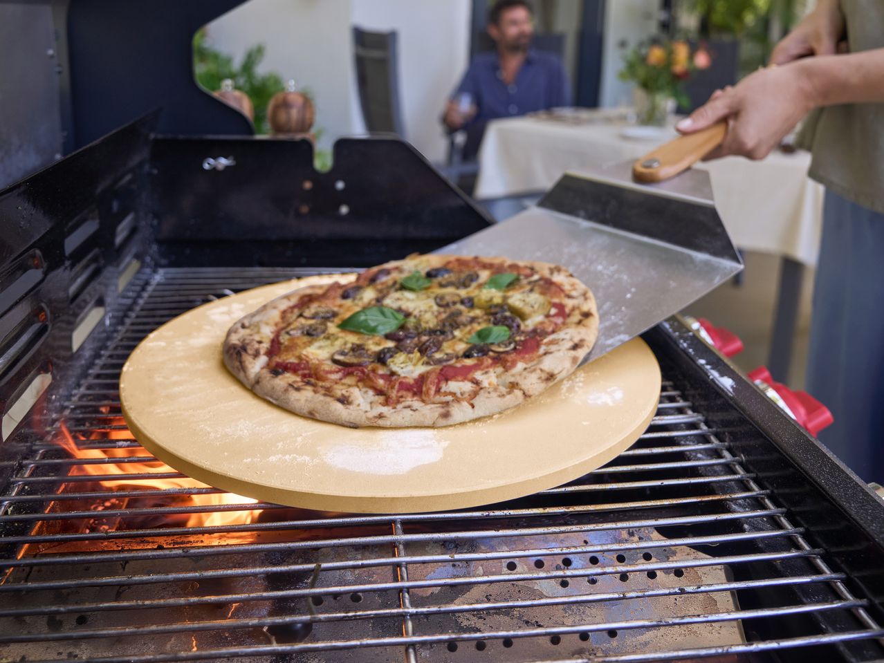 Πίτσα σε πέτρα πίτσας τοποθετείται σε ψησταριά μπάρμπεκιου με φτυάρι πίτσας.