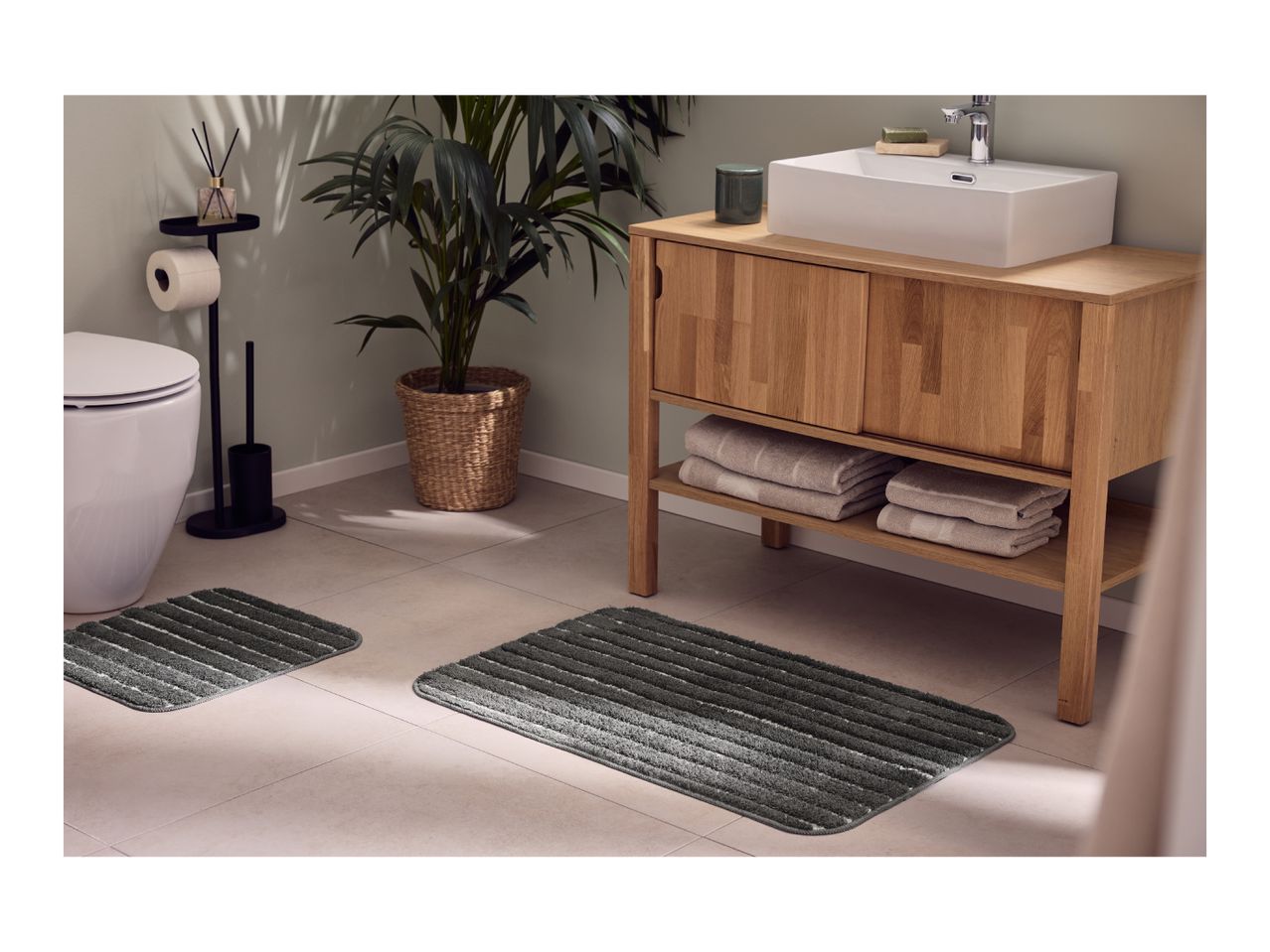 Bathroom with wooden vanity, white sink, toilet, and dark grey striped bath mats.
