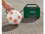 A person inflating a white and orange soccer ball with a green portable air compressor.
