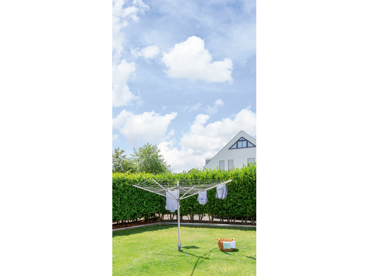 Rotary clothesline with laundry drying in a sunny garden with a house in the background.