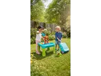 Two children playing with a water and sand table, a bubble machine, and a toy suitcase in a garden.