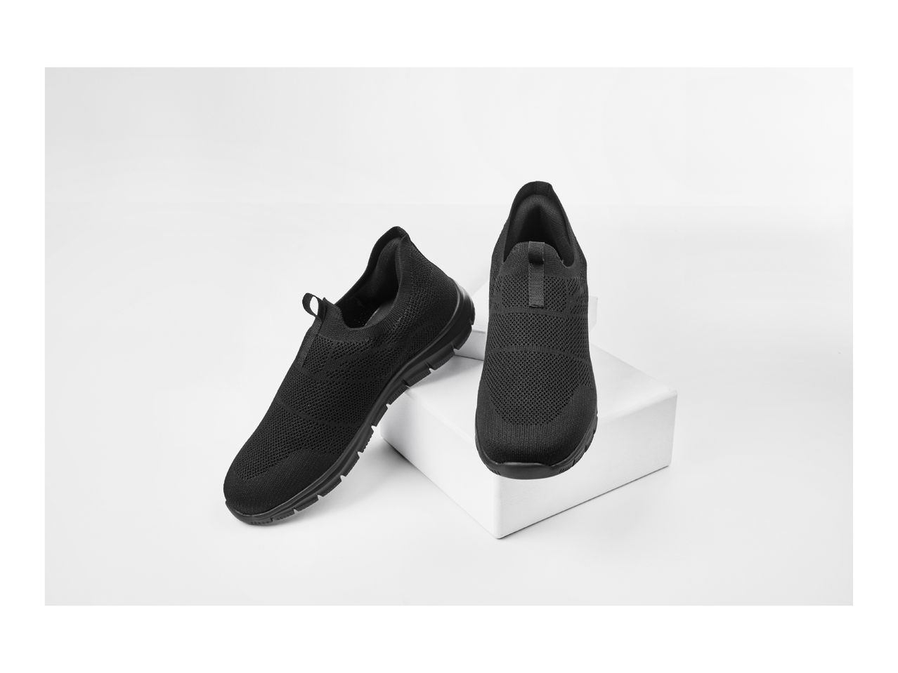 Pair of black slip-on sneakers on a white display stand
