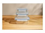 Three clear glass food storage containers with blue lids stacked on a wooden surface.