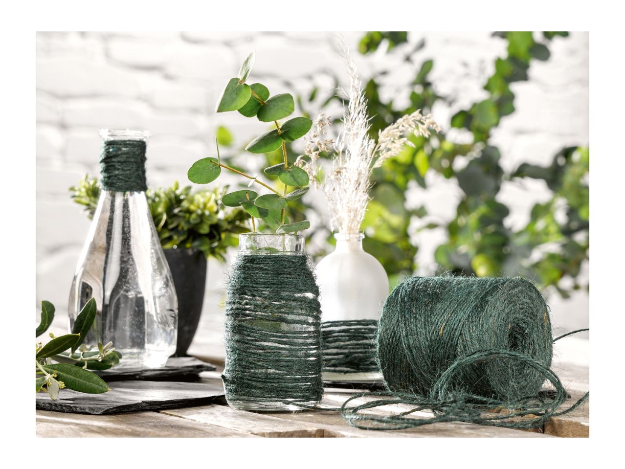 Green jute twine roll next to decorated glass vases with plants on a wooden table