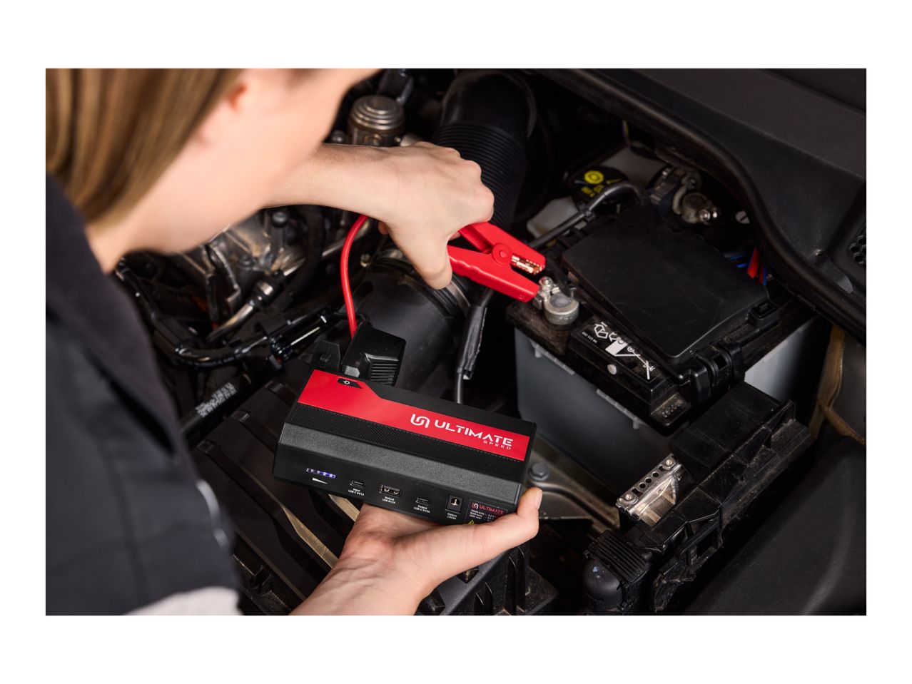 A person jump-starting a car battery with a portable jump starter.