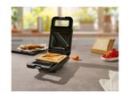 A sandwich maker with a toasted sandwich inside, on a kitchen counter.