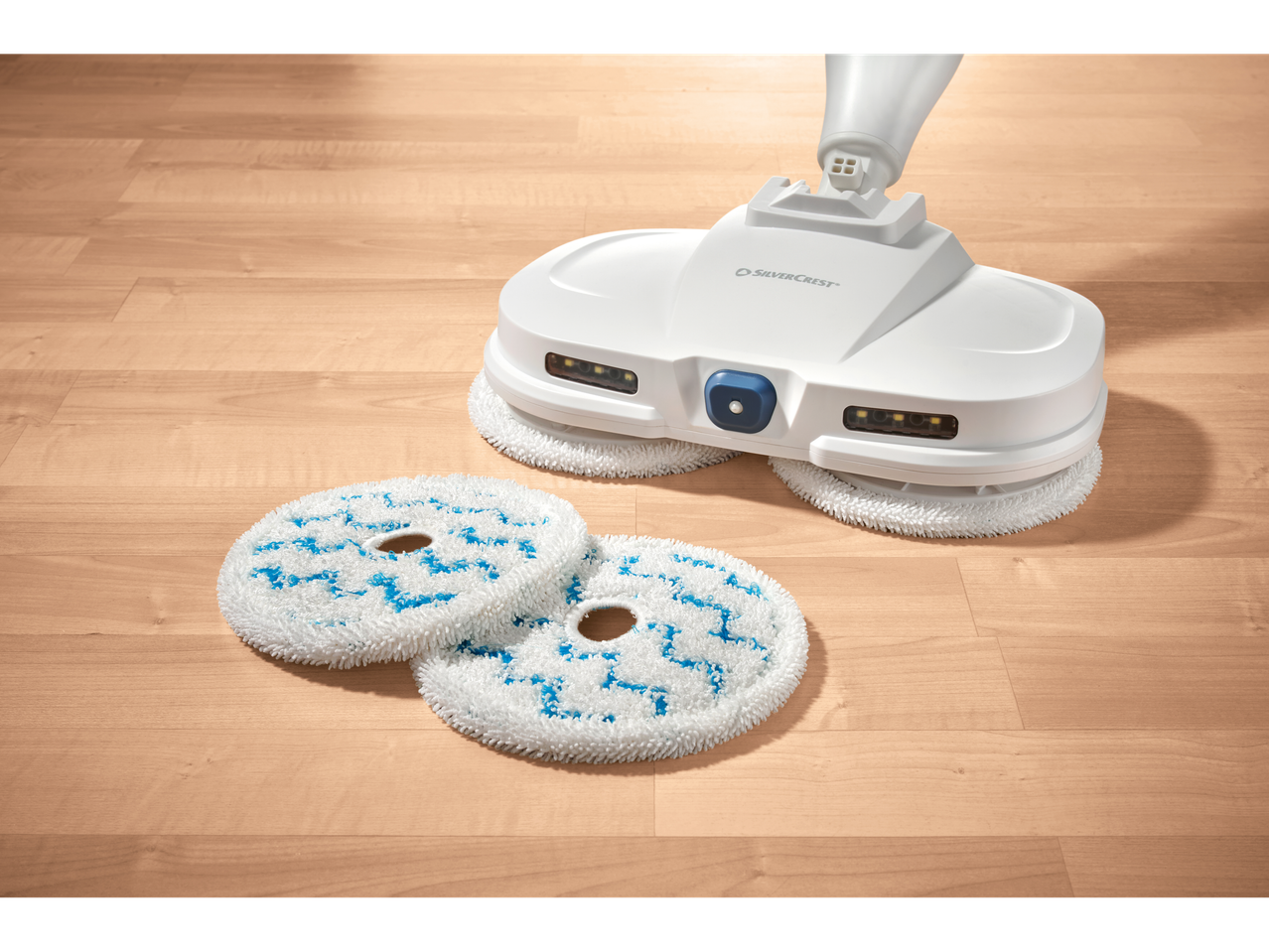 Mopa elétrica Silvercrest® com função de pulverização e duas almofadas de limpeza num chão de madeira.