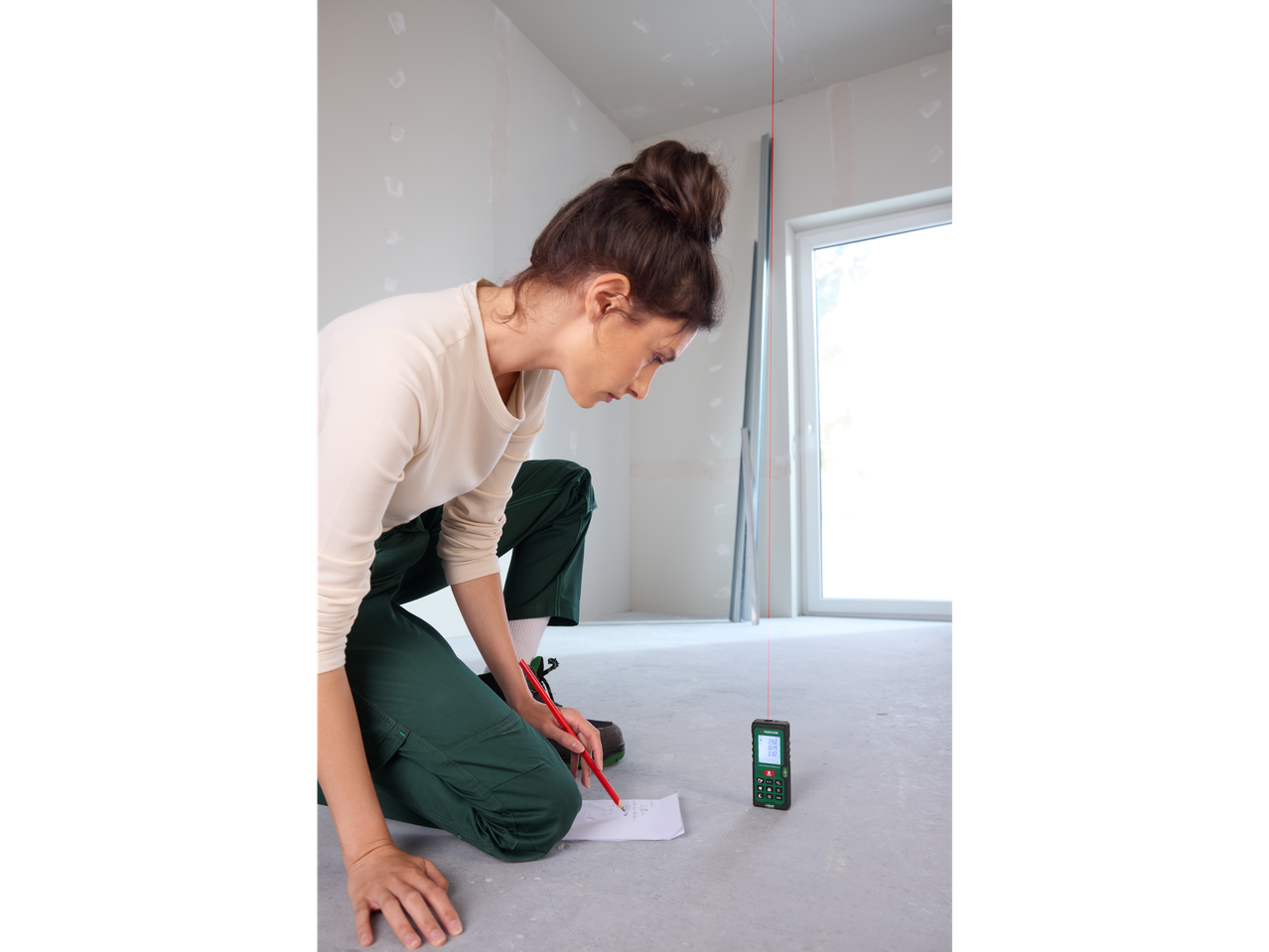 A woman uses a PARKSIDE® Laser Distance Measurer in a room under construction.