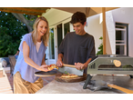 Grillmeister Pizza Cutter and Pizza Peel Paddle in use by two people outdoors.