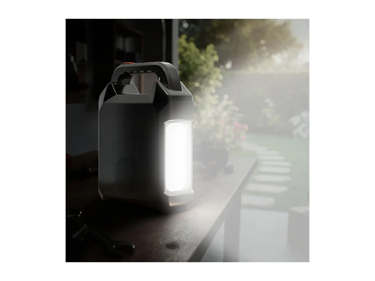 Portable work light on a wooden table in a garden setting.