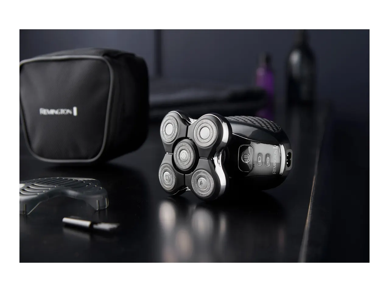 Electric shaver with multiple rotary blades, a travel bag, and accessories on a dark surface.