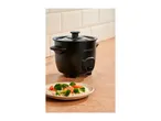 Black rice cooker on a wooden counter with a plate of rice and vegetables.