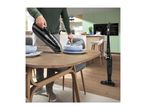 Man using a handheld vacuum cleaner to clean crumbs off a wooden dining table.