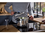 Man in a modern kitchen opening a stainless steel pressure cooker on an induction hob.