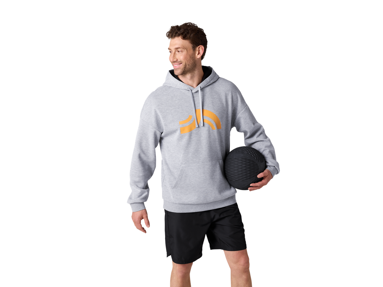 Mees hallis CRIVIT kapuutsiga pusas oranži logoga ja mustade lühikeste pükstega, hoides musta palli.