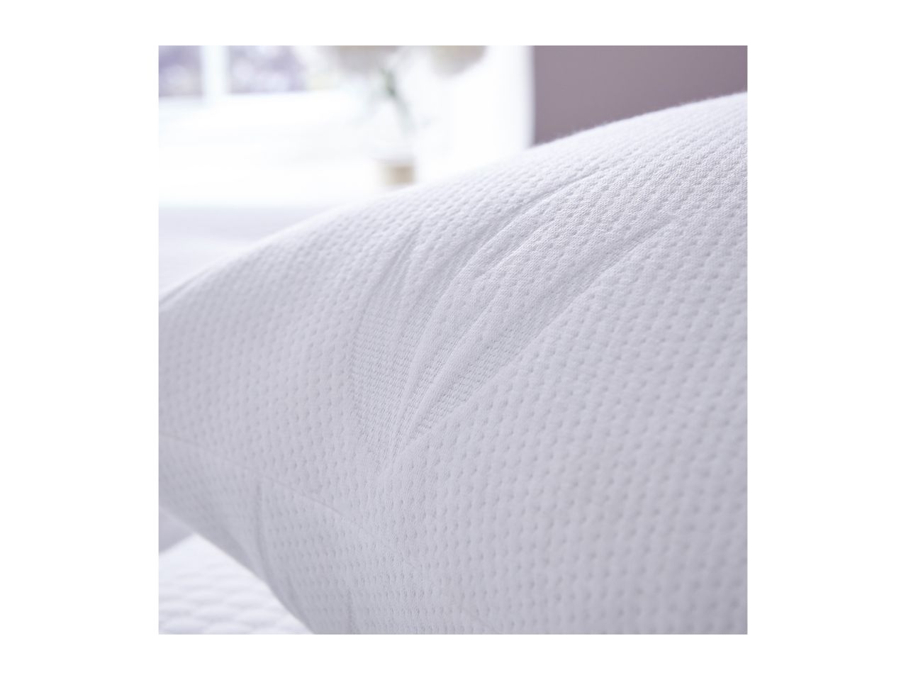 Close-up of a white textured pillow with a subtle pattern, in a bright room.