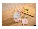 Pink blender with ice cubes, limes, raspberries, and a drink on a wooden counter.