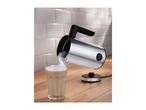 Stainless steel milk frother pouring frothed milk into a glass on a wooden counter