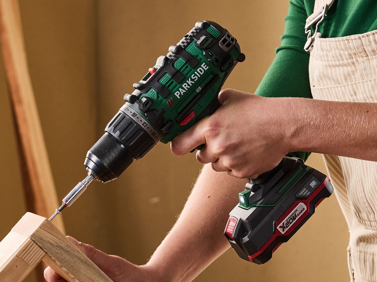 A person using a cordless drill to screw into a piece of wood.
