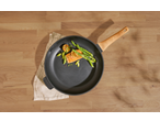 Cooked salmon with asparagus and lemon in a frying pan on a wooden surface.