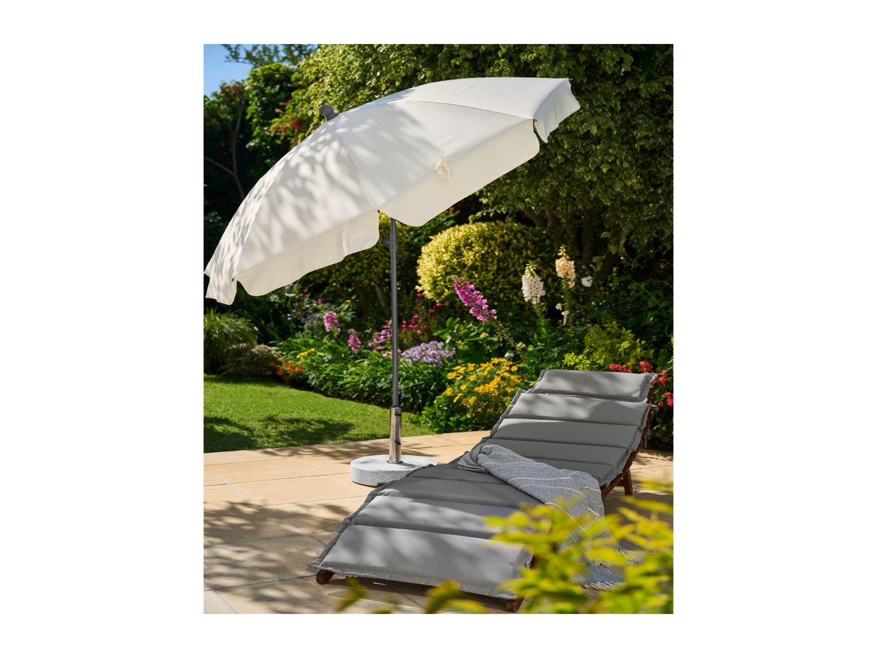 Garden lounger with grey cushions and a white parasol on a patio.