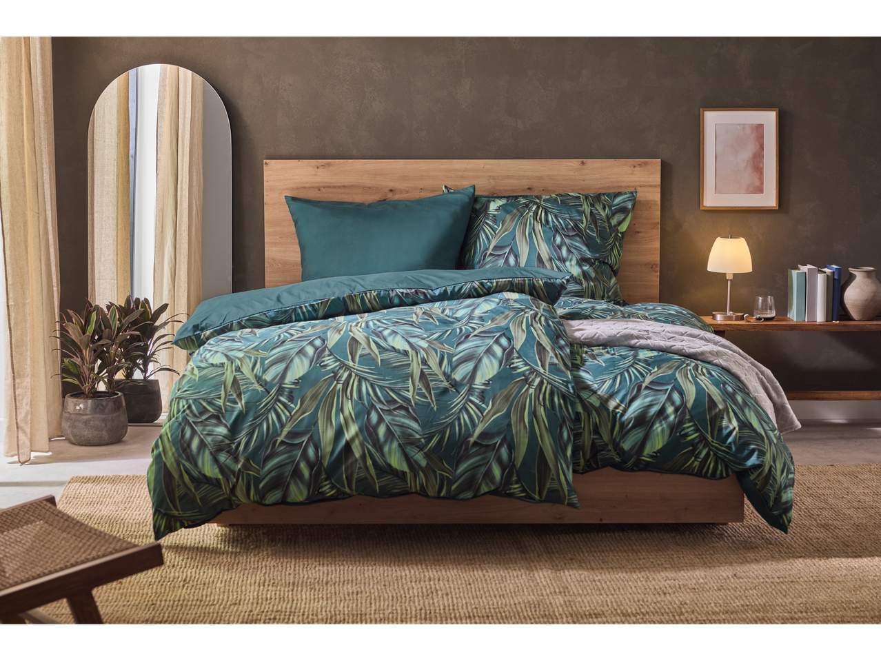 Slaapkamer met beddengoed met tropische bladeren, een houten bed en een spiegel.