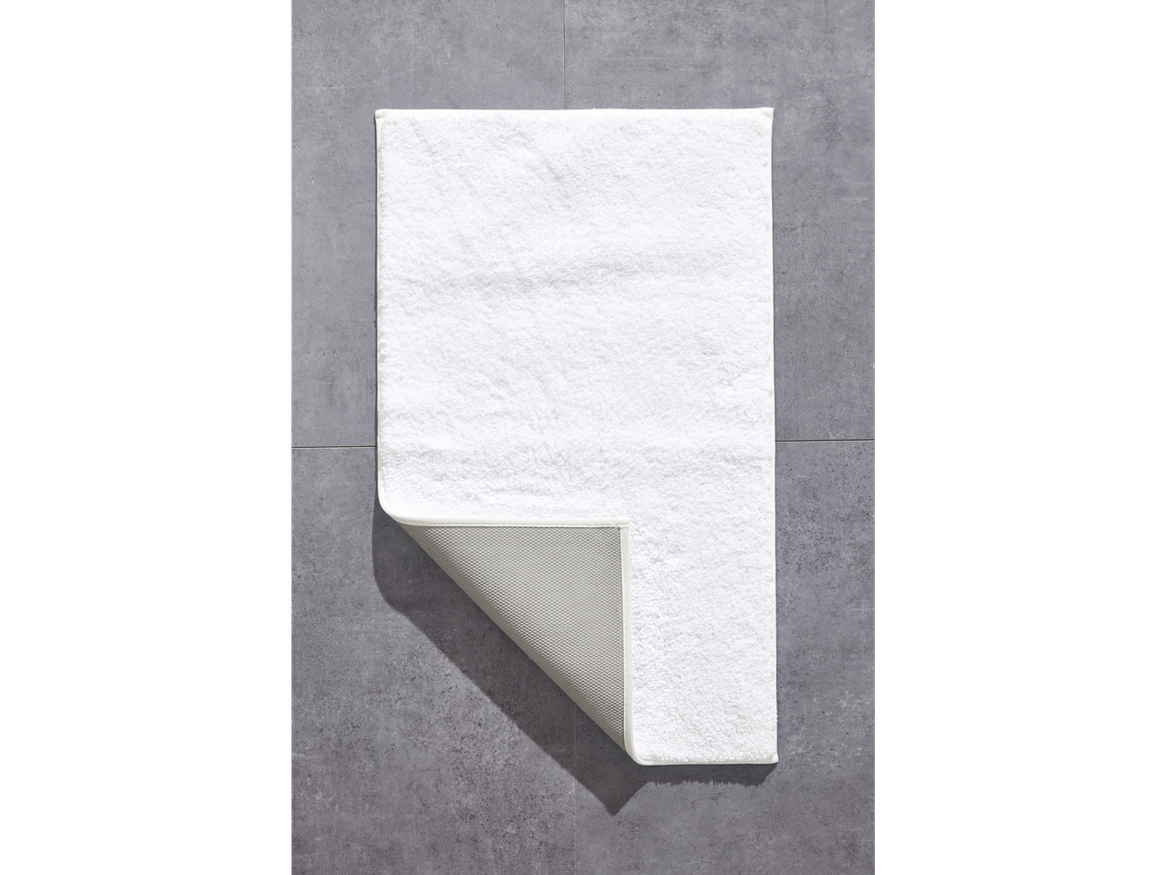 Een wit badmat op een grijze vloer.