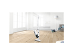A white Bosch cordless vacuum cleaner stands on a light wooden floor in a bright room.