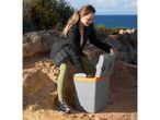 Woman opening a portable cooler on a rocky coastal path with the sea in the background.
