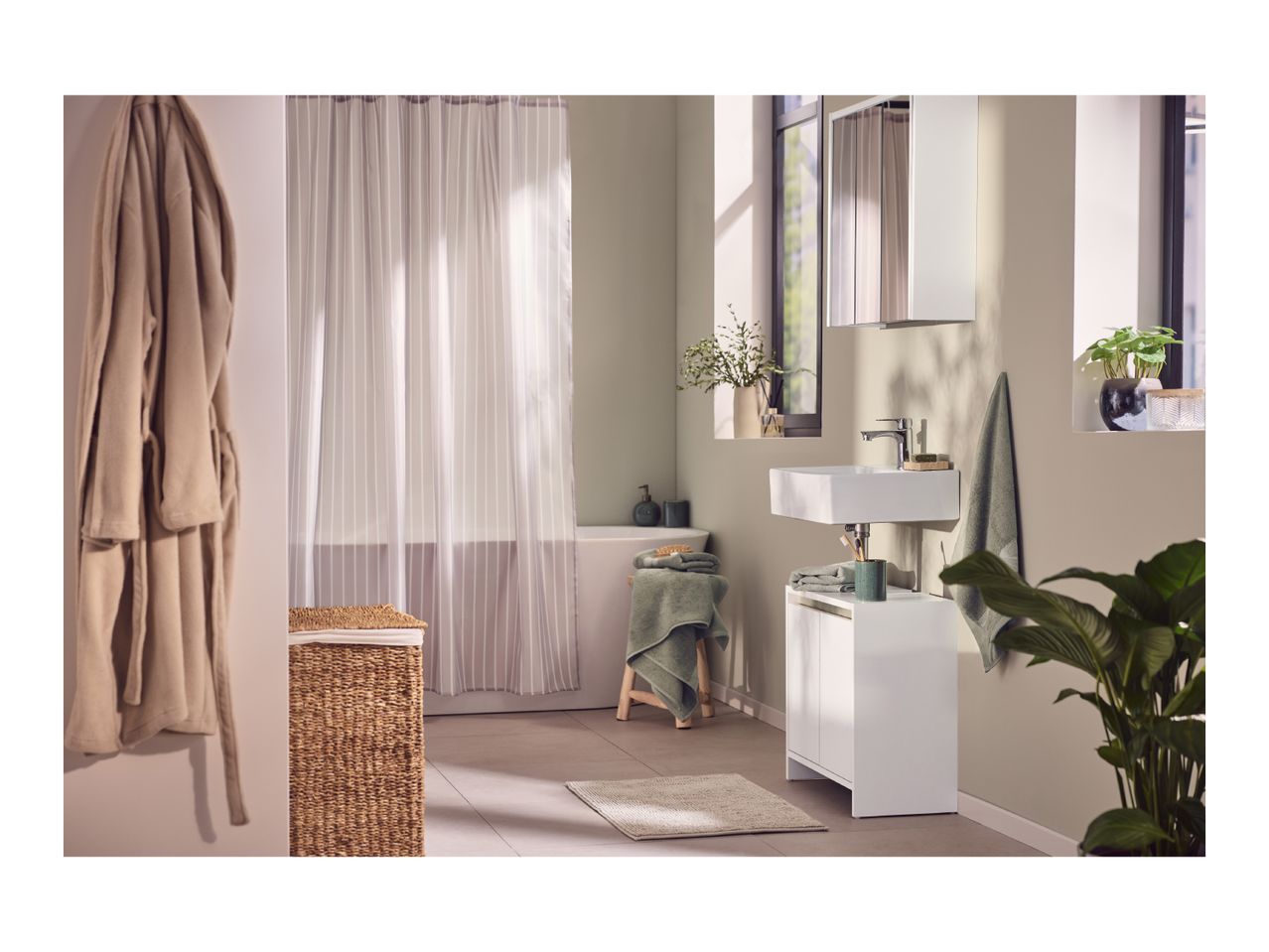 A modern bathroom with a white sink, cabinet, and bathtub, featuring green towels and plants.