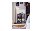 Floor lamp illuminating a dark green serving trolley with coffee accessories.