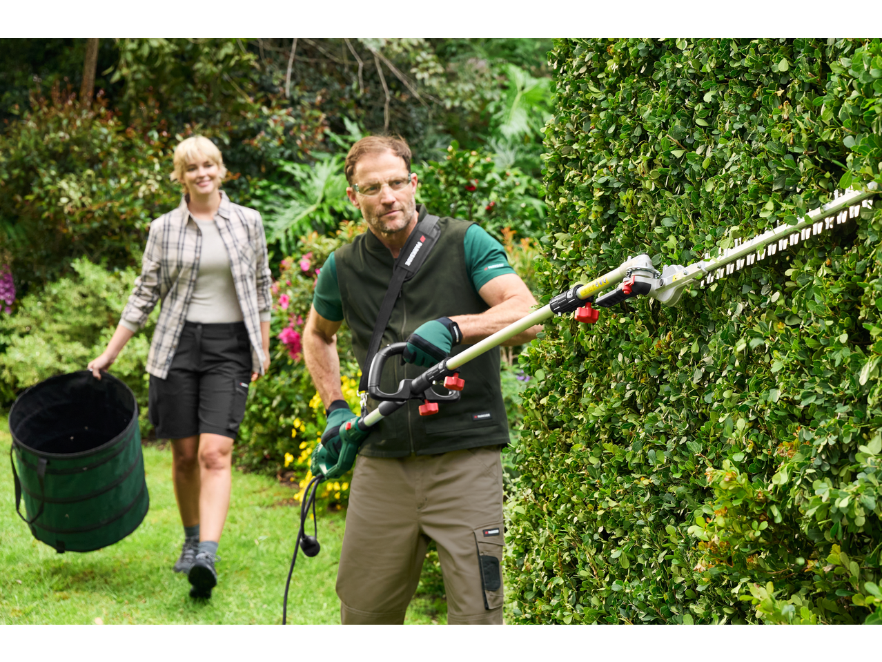 Man in PARKSIDE work trousers trimming a hedge, woman with a garden bag.