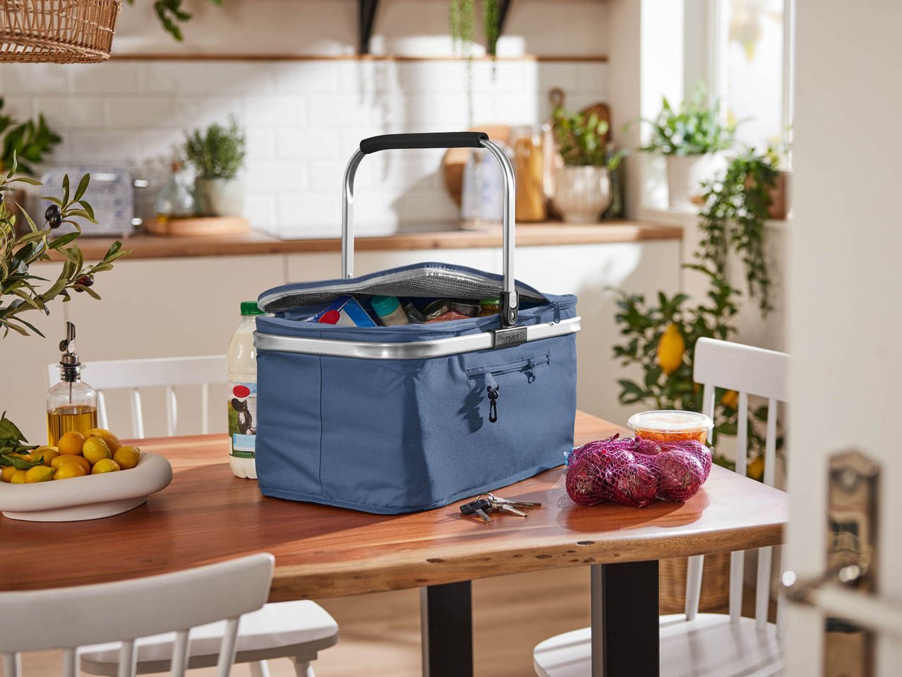 A blue cooler bag filled with groceries on a wooden table in a kitchen.
